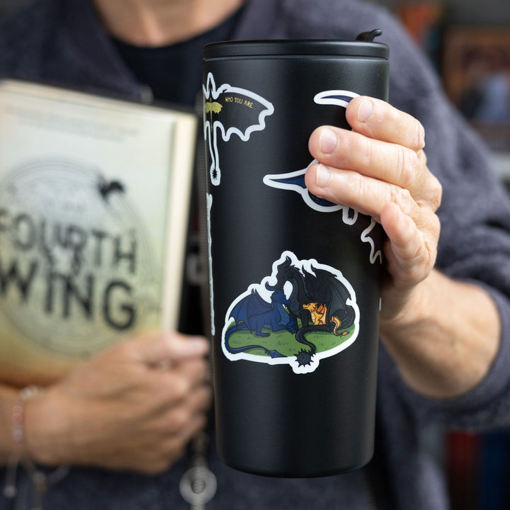 Sticker of 3 dragons - a blue and a black adult with a golden baby dragon - cuddled up like a family, as a sticker, on a black tumbler. 
