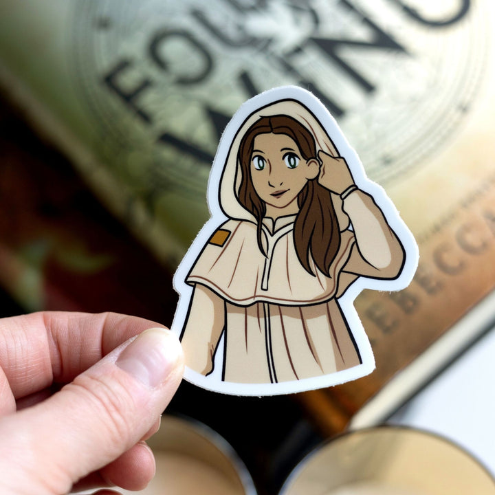 Sticker of Jesinia the scribe from Fourth Wing. She has long, brown hair & cream colored robes with the hood up, held over Fourth Wing