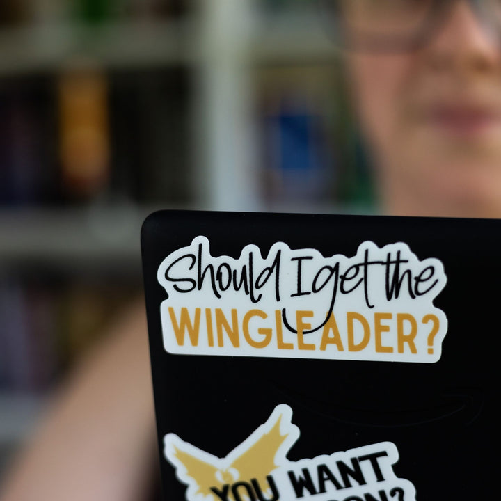 Fourth Wing quote sticker: ‘ Should I get the wingleader’ in black and gold colors. On a laptop.