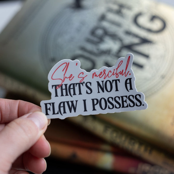 Quote sticker: ‘She’s merciful. That’s not a flaw I possess’ in red and black letters, held over Fourth Wing.
