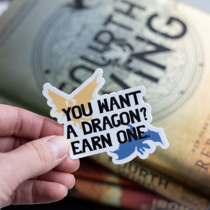  Sticker with a golden and blue dragon in each corner that says ‘You want a dragon? Earn one’ in black letters. Held over Fourth Wing.
