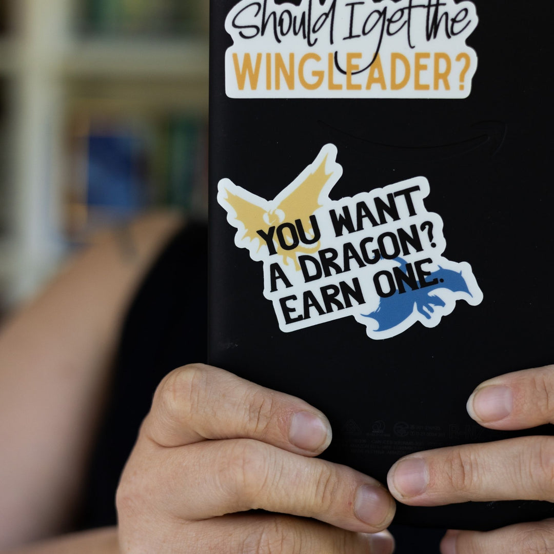 Sticker with a golden and blue dragon in each corner that says ‘You want a dragon? Earn one’ in black letters. On a black e-reader.