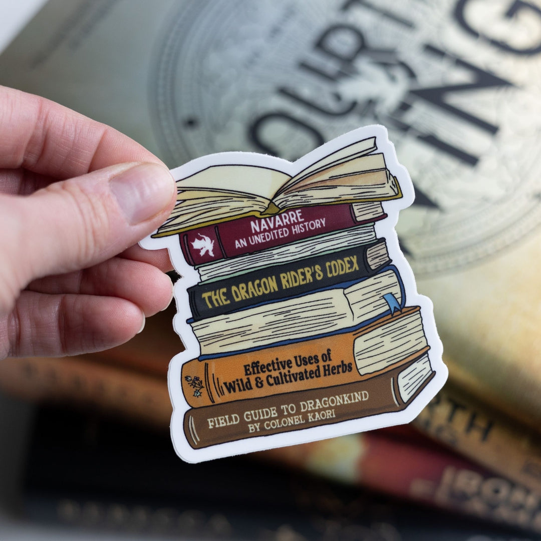  Sticker of a stack of books spines from Fourth Wing, like ‘Navarre: An Unedited History,’ and ‘The Dragon Rider’s Codex.’ Held over Fourth Wing.