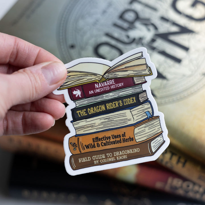  Sticker of a stack of books spines from Fourth Wing, like ‘Navarre: An Unedited History,’ and ‘The Dragon Rider’s Codex.’ Held over Fourth Wing.
