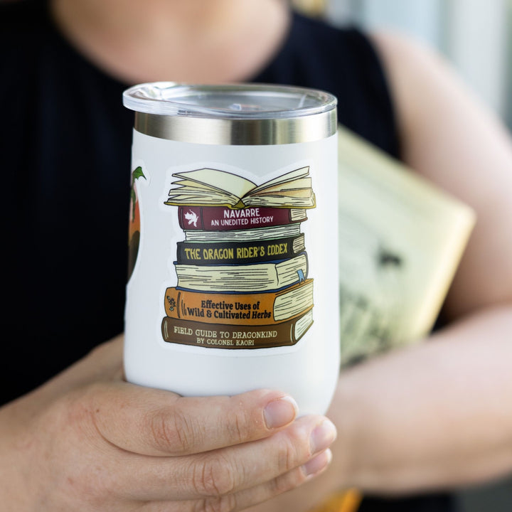 Sticker of a stack of books spines from Fourth Wing, like ‘Navarre: An Unedited History,’ and ‘The Dragon Rider’s Codex.’ On a white tumbler.
