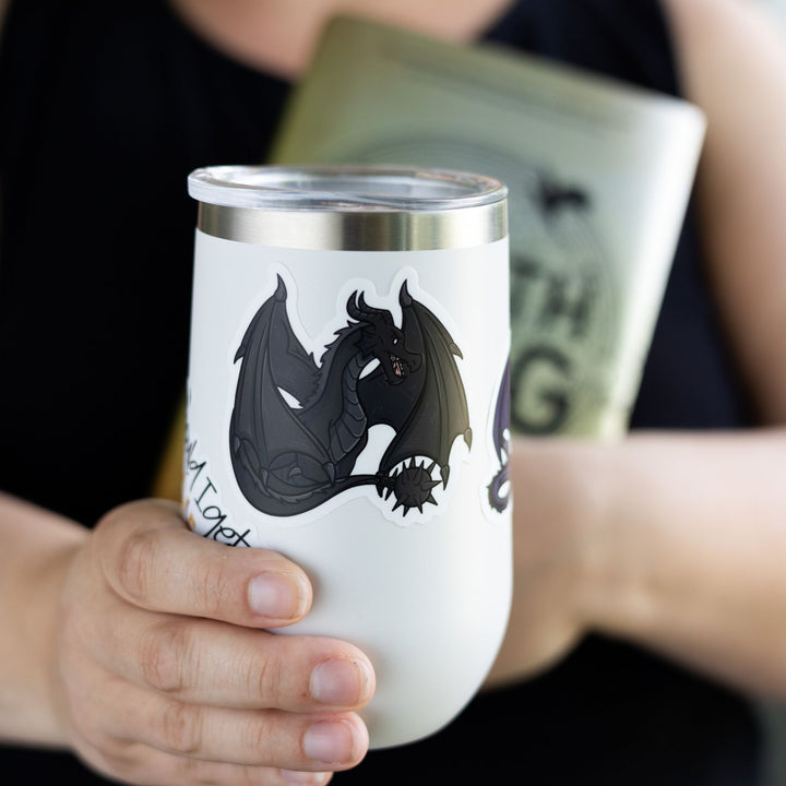 Tairn, black dragon from Fourth Wing by Rebecca Yarros, sitting with tail and wings tucked around him on white tumbler.