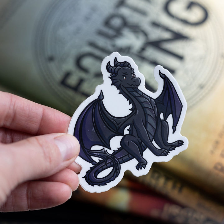 Sticker of a teenage Andarna, a black dragon who is sitting proudly, tail curled. Held over Fourth Wing