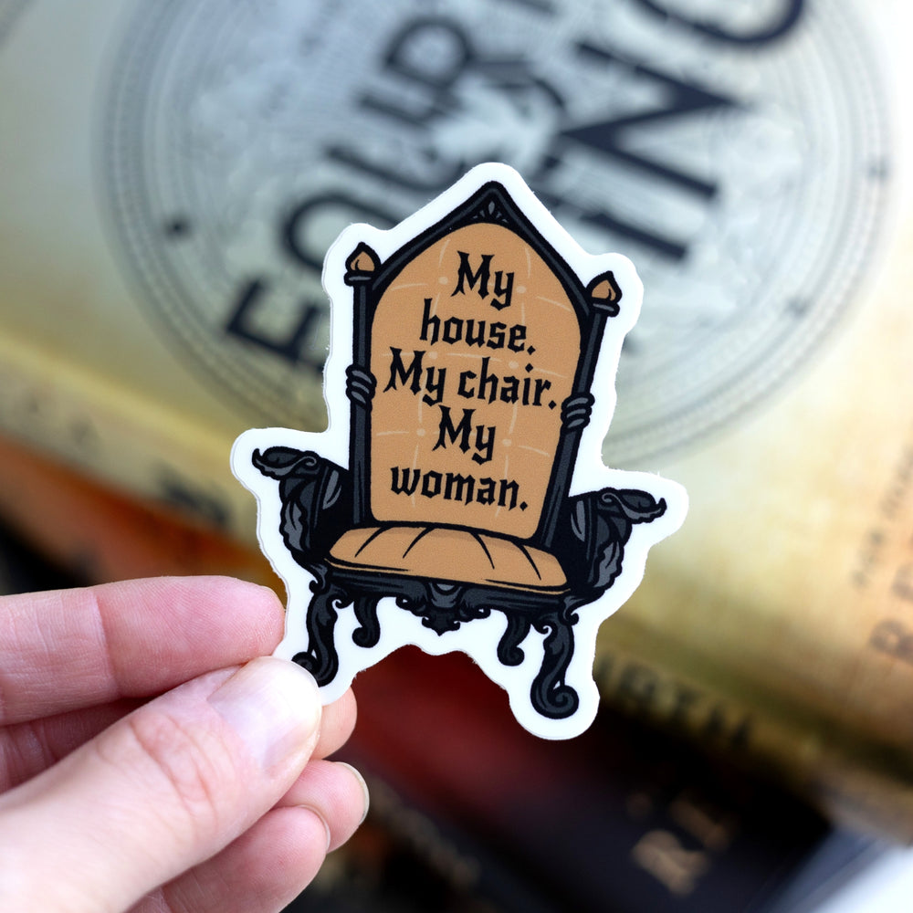 Sticker of chair with dark gold upholstery with the Fourth Wing quote: ‘My house. My chair. My woman’ held over Fourth Wing.