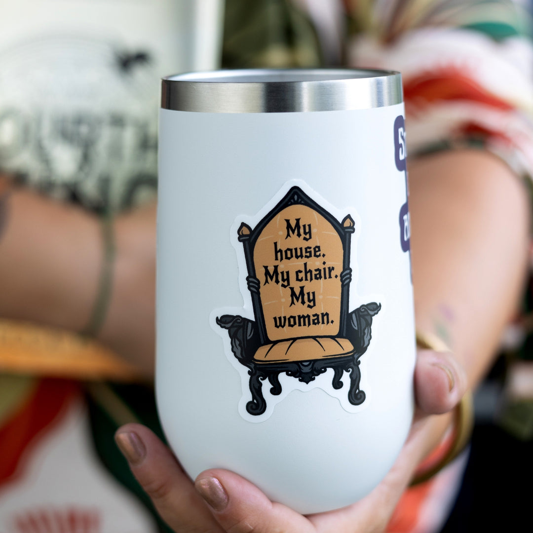 Sticker of chair with dark gold upholstery with the Fourth Wing quote: ‘My house. My chair. My woman.’ On a white tumbler. 