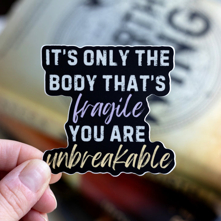  Fourth Wing quote sticker: ‘It’s only the body that’s fragile you are unbreakable.’ Words are light gray but ‘fragile’ is purple and ‘unbreakable’ is gold. Held over Fourth Wing.