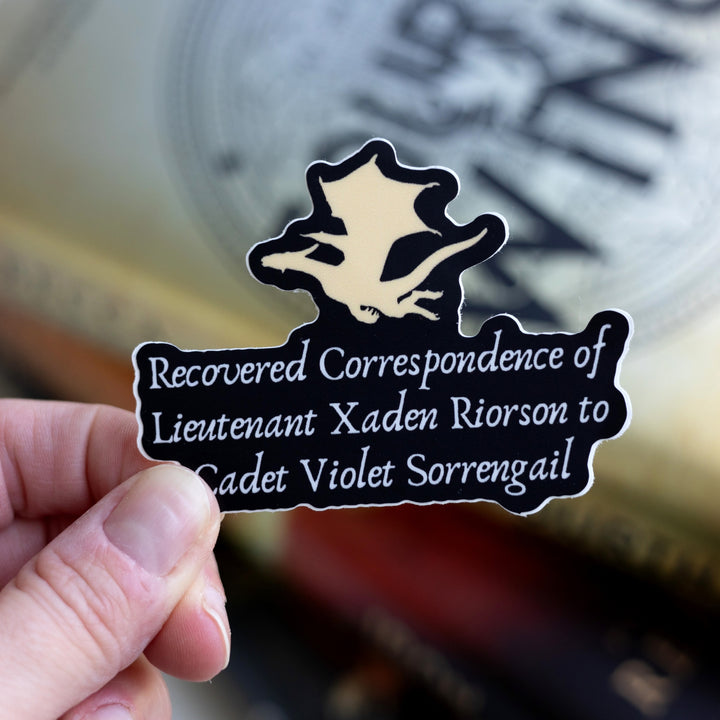  Sticker of a gold dragon flying over the words ‘Recovered correspondence of Lieutenant Xaden Riorson to Cadet Violet Sorrengail.’ Held over Fourth Wing. 