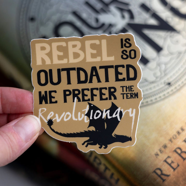 Sticker that reads ‘Rebel is so outdated we prefer the term revolutionary’. On a yellow background with a black dragon flying underneath. Held above Fourth Wing.
