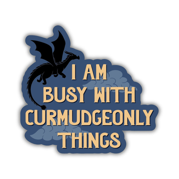 Sticker that reads ‘ I am busy with curmudgeonly things’. With clouds and a black dragon flying over the words.