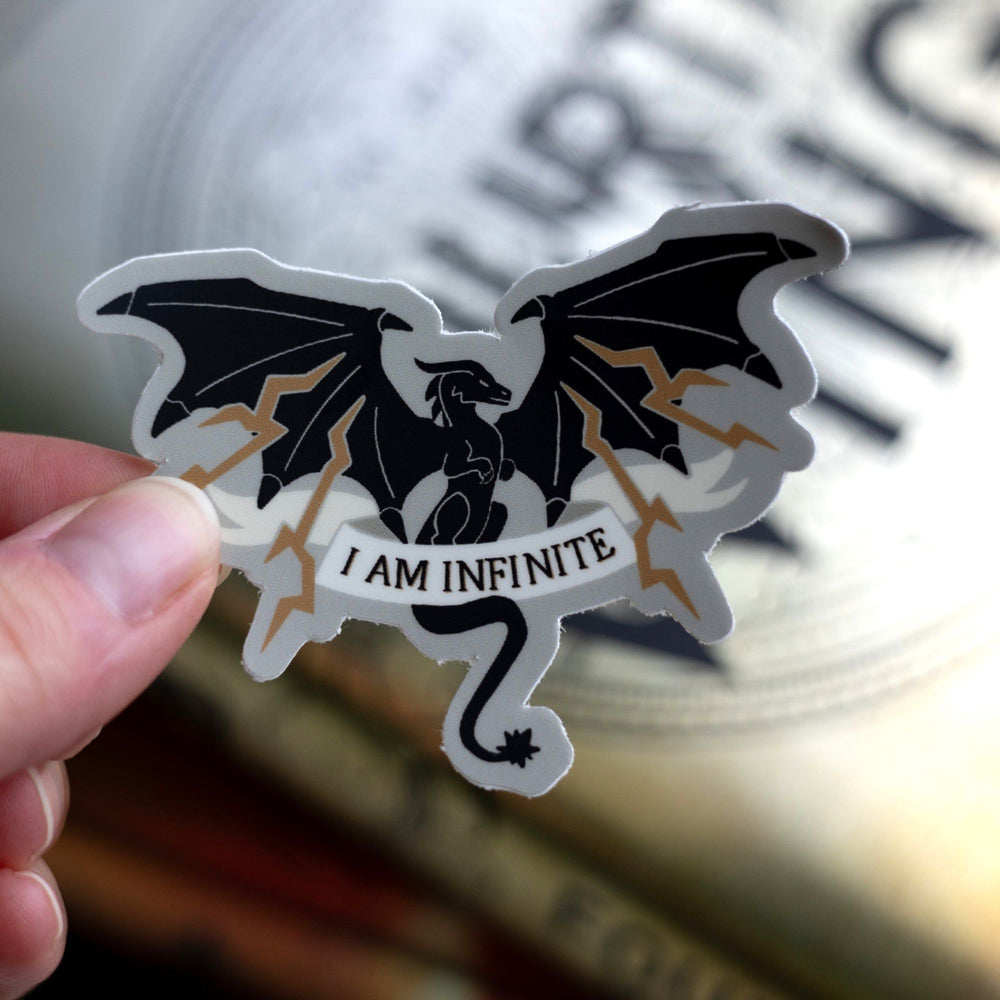 Sticker of a black dragon with lighting coming out of its wings with the words ‘ I am infinite’ on an ivory ribbon over its tail. Held above Fourth Wing.
