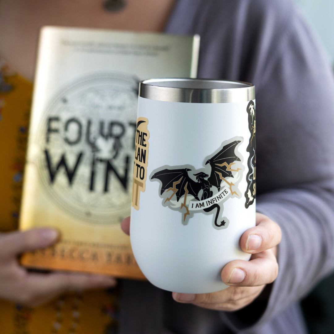 Sticker of a black dragon with lighting coming out of its wings with the words ‘ I am infinite’ on an ivory ribbon over its tail. On a white tumbler.
