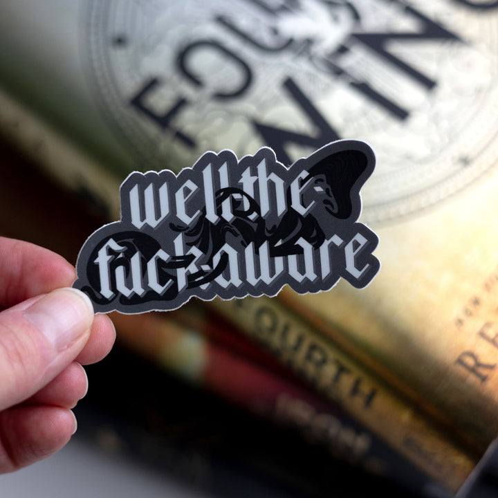 Quote sticker from Fourth Wing by Rebecca Yarros that reads ‘ Well-the-fuck-aware’ with Xaden’s shadows. Held above Fourth Wing.
