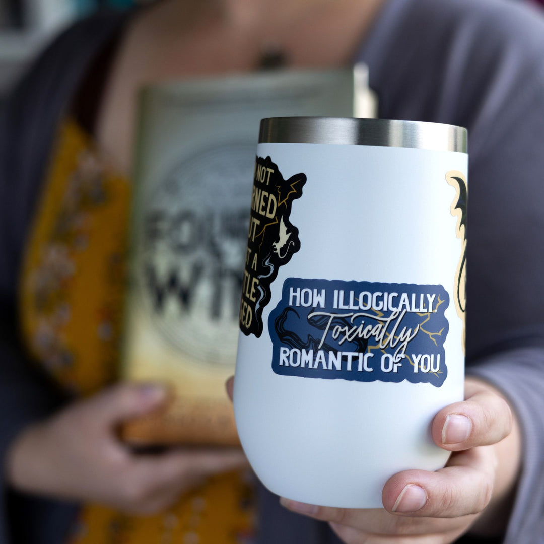 Quote sticker from Onyx Storm reads ‘How illogically, toxically romantic of you’ with shadows and lightning. On a white tumbler.

