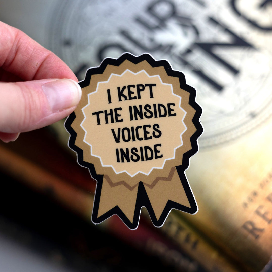  A sticker of a gold ribbon that reads ‘I kept the inside voices inside’. Held above Fourth Wing.
