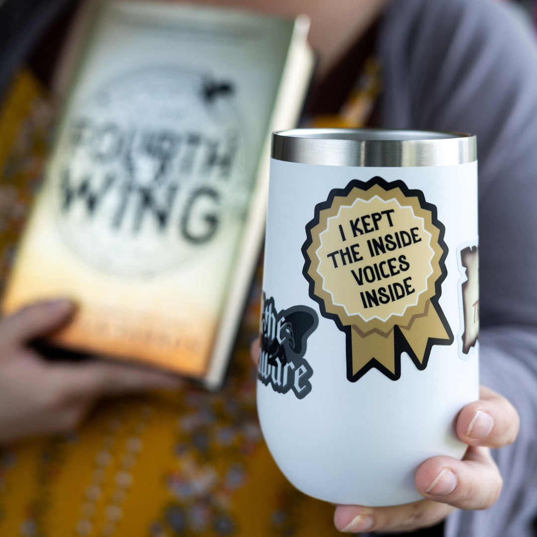   A sticker of a gold ribbon that reads ‘I kept the inside voices inside’. On a white tumbler.
