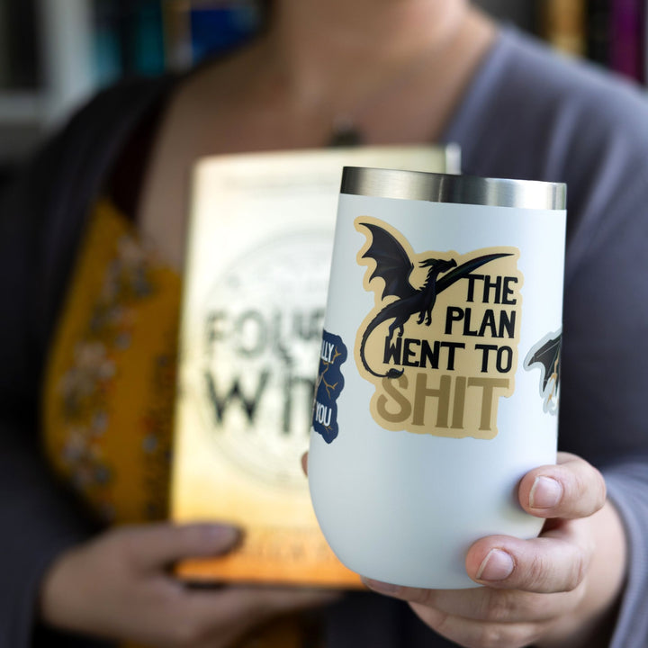  Sticker of an iridescent dragon in flight with text ‘The plan went to shit’. On a white tumbler.
