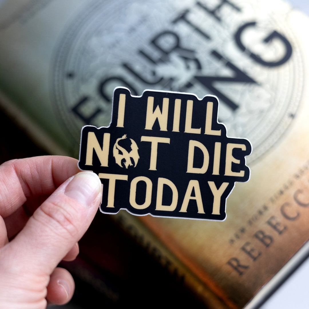 Sticker of Violet Sorrengail’s mantra ‘I will not die today’ in gold text on a black background. Sticker is held over Fourth Wing.