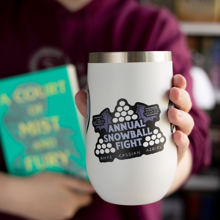 Sticker for the ACOTAR ‘Annual Snowball Fight.’ The words are surrounded by three piles of snowballs and bat wings. ‘Rhys Cassian Azriel’ is on the bottom. On a white tumbler.
