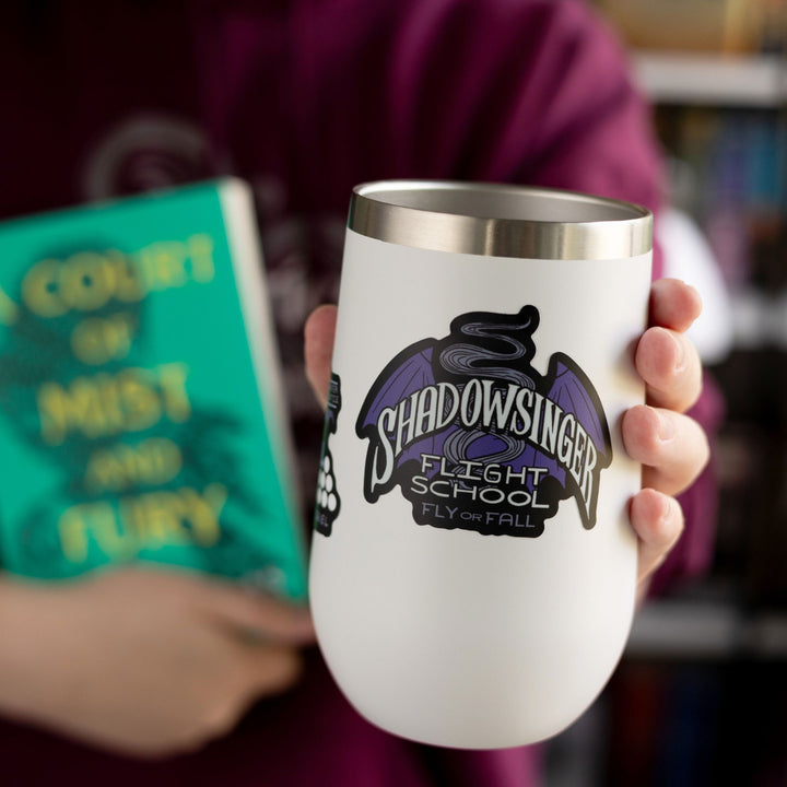 Sticker of purple bat wings that says ‘Shadowsinger Flights school, fly or fall.’ Inspired by ACOTAR. On a white tumbler.