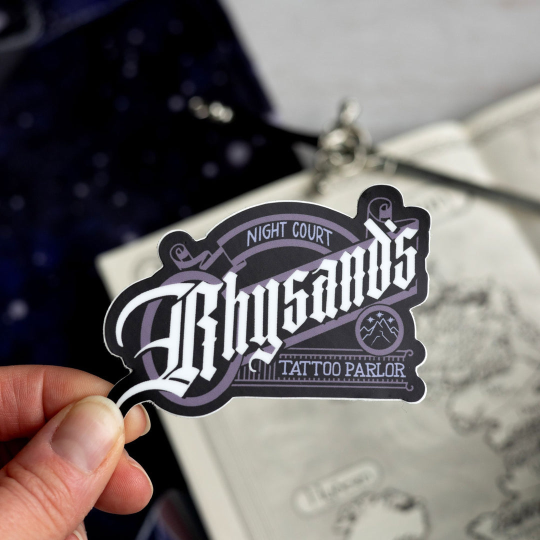  Sticker that looks like a classic style logo and reads ‘Night court, Rhysand’s Tattoo Parlor.’ Held above a map.