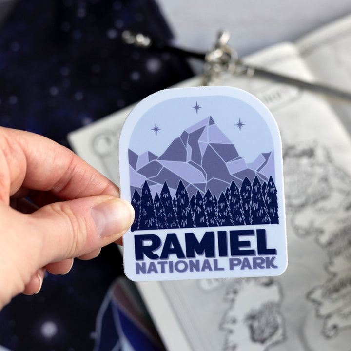  Sticker of a mountain with three stars above it and evergreen trees. Below reads ‘Ramiel National Park.’  Held above a map.
