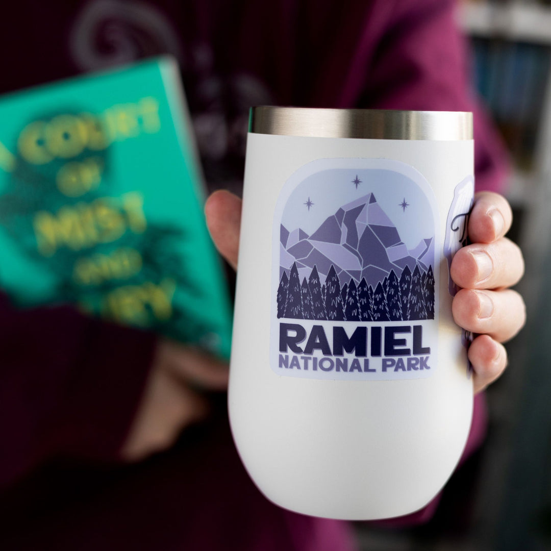 Sticker of a mountain with three stars above it and evergreen trees. Below reads ‘ Ramiel National Park.’ Inspired by ACOTAR. On a white tumbler.
