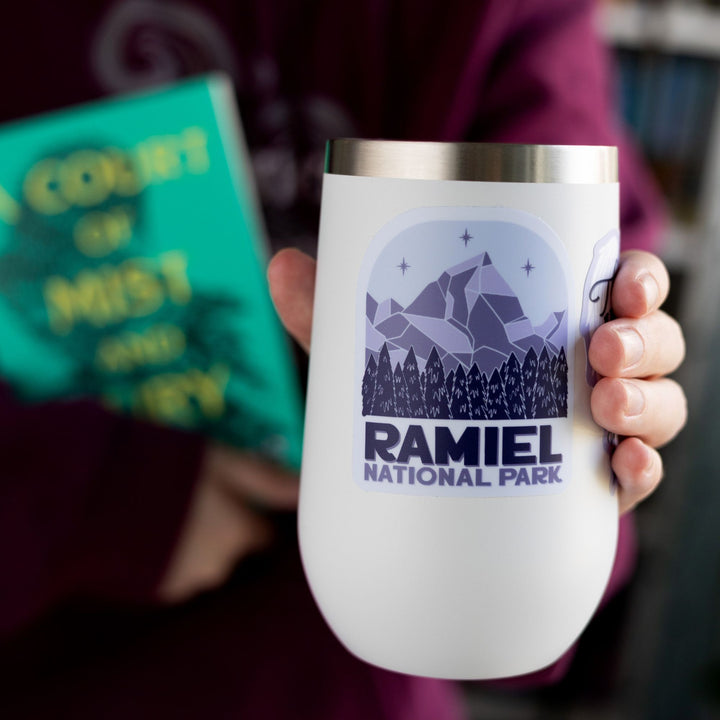 Sticker of a mountain with three stars above it and evergreen trees. Below reads ‘ Ramiel National Park.’ Inspired by ACOTAR. On a white tumbler.
