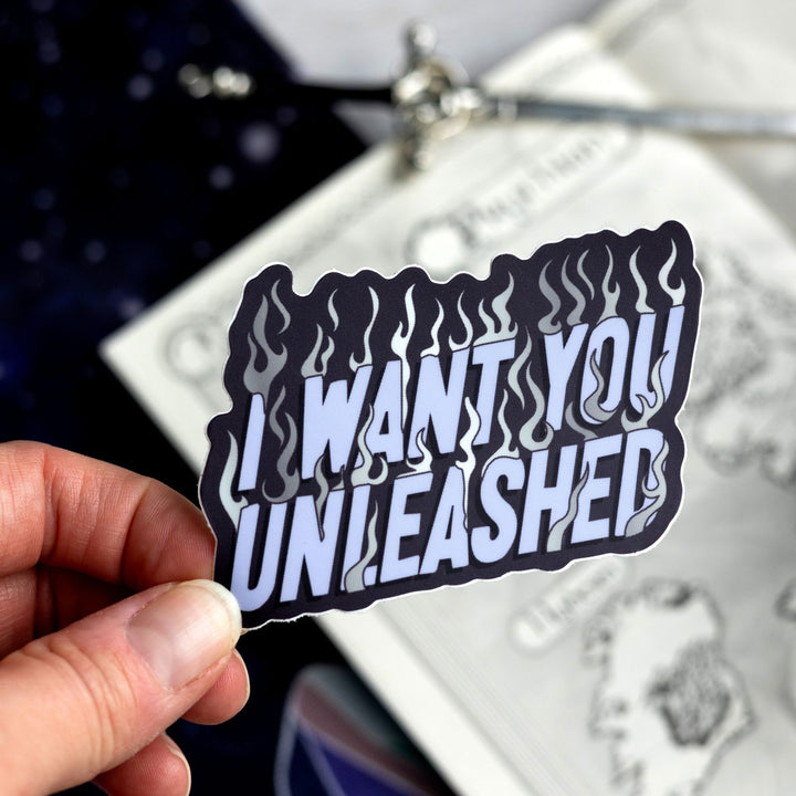 ACOTAR quote sticker ‘I want you unleashed’ in purple letters and silver flames. Held above a map.
