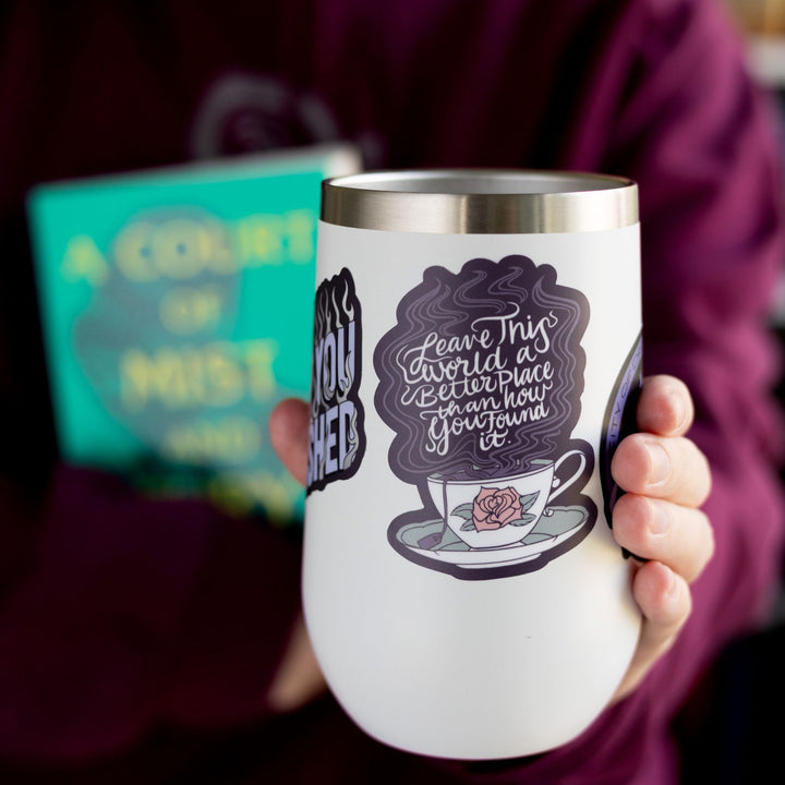  ACOTAR quote sticker ‘Leave this world a better place than how you found it’ above a steaming white teacup with a rose on it. On a white tumbler.