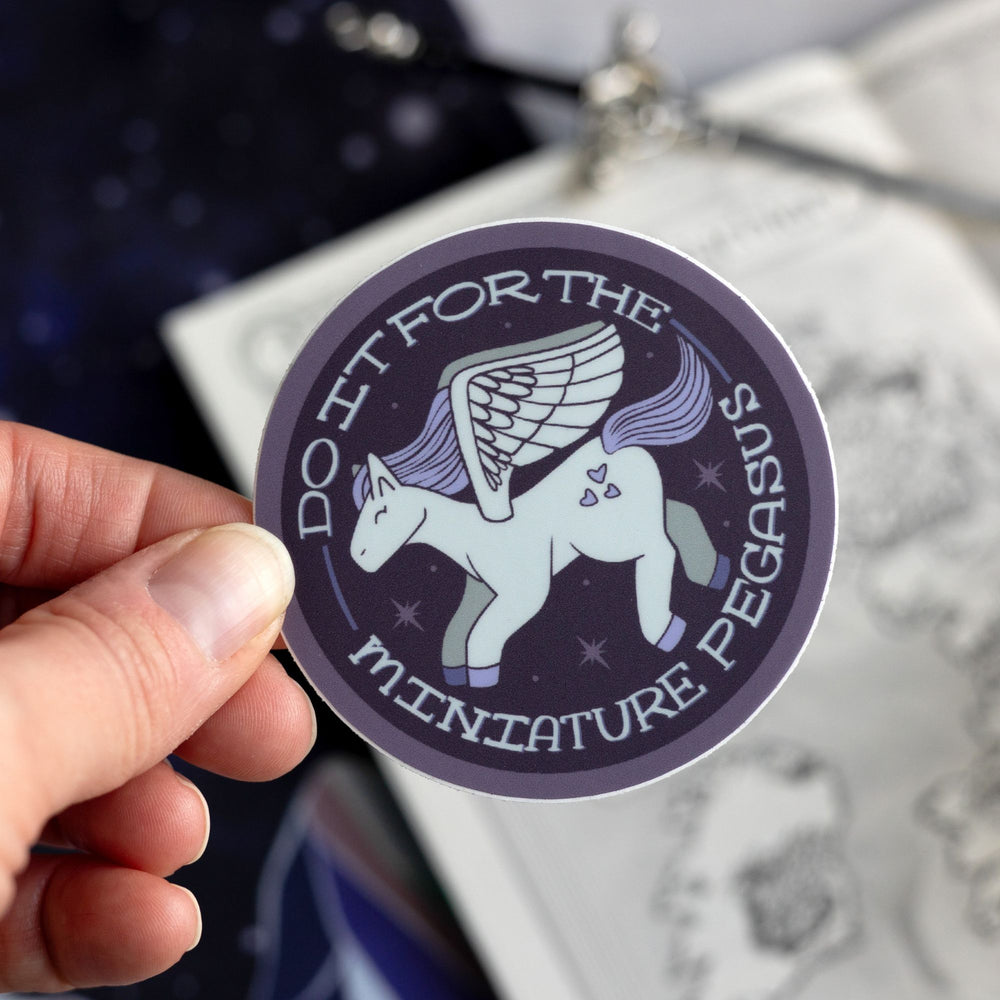 Sticker of a white and purple pegasus that says ‘Do it for the miniature pegasus around the circle. Held above a map.
