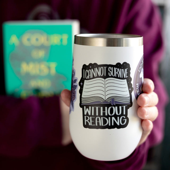 ACOTAR quote sticker ‘I cannot survive without reading’ and an open book with a purple ribbon bookmark. On a white tumbler.
