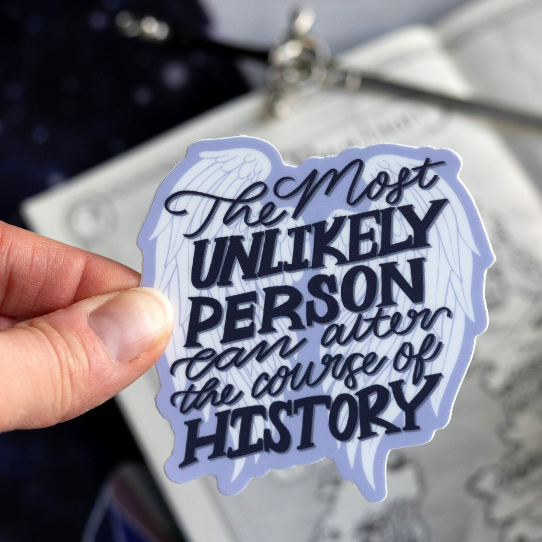 ACOTAR quote sticker ‘The most unlikely person can alter the course of history’ on a pair of white angel wings outlined in purple. Held above a map.