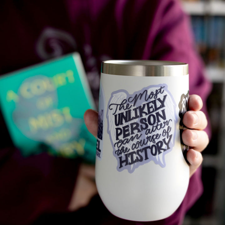  ACOTAR quote sticker ‘The most unlikely person can alter the course of history’ on a pair of white angel wings outlined in purple. On a  white tumbler.
