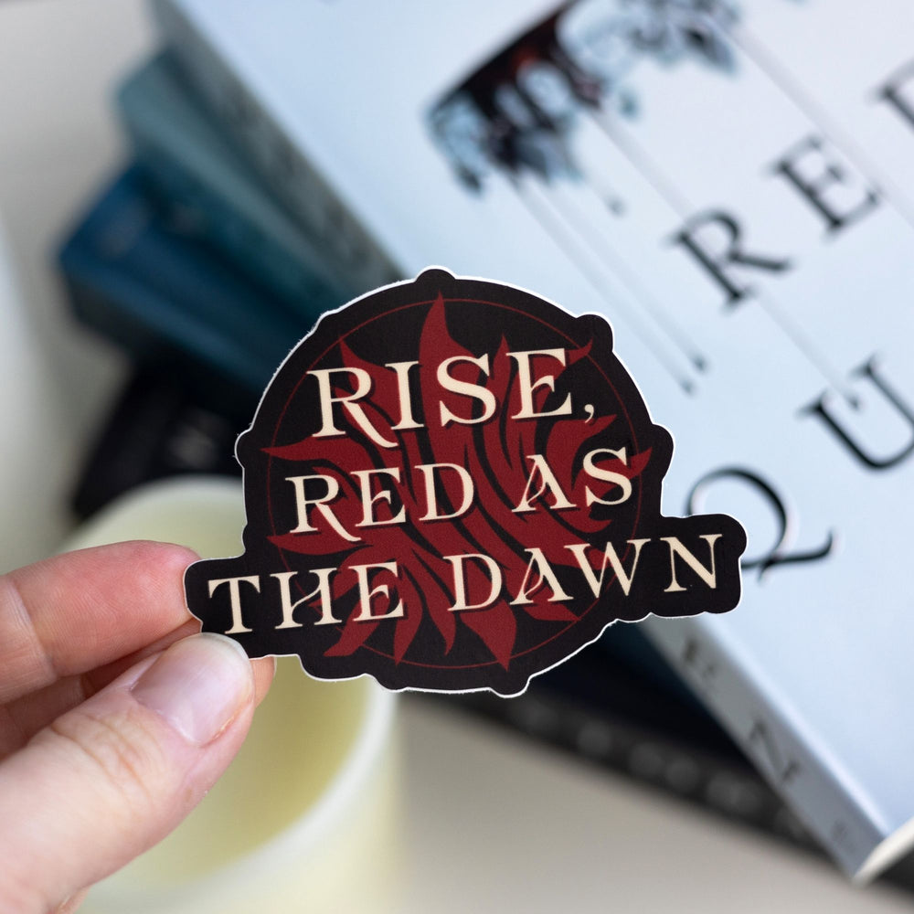 ‘Rise, Red as the dawn’ in gold over an exploding red sun, the symbol of the Scarlet Guard. Held over Red Queen.