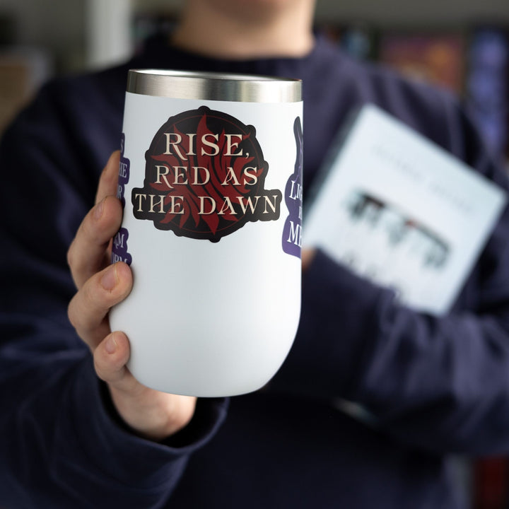 Red Queen quote sticker on a white tumbler: Text says ‘Rise, Red as the dawn’ in gold over an exploding red sun, the symbol of the Scarlet Guard.