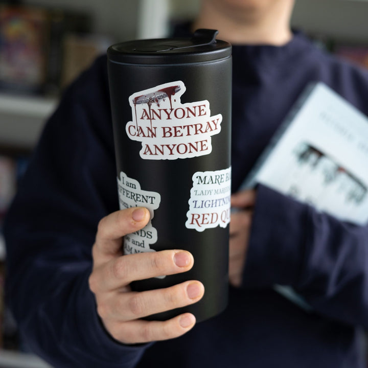 Red Queen quote sticker on a tall black tumbler. Text is ‘Anyone can betray anyone’ in red beneath an upside down crown dripping blood.