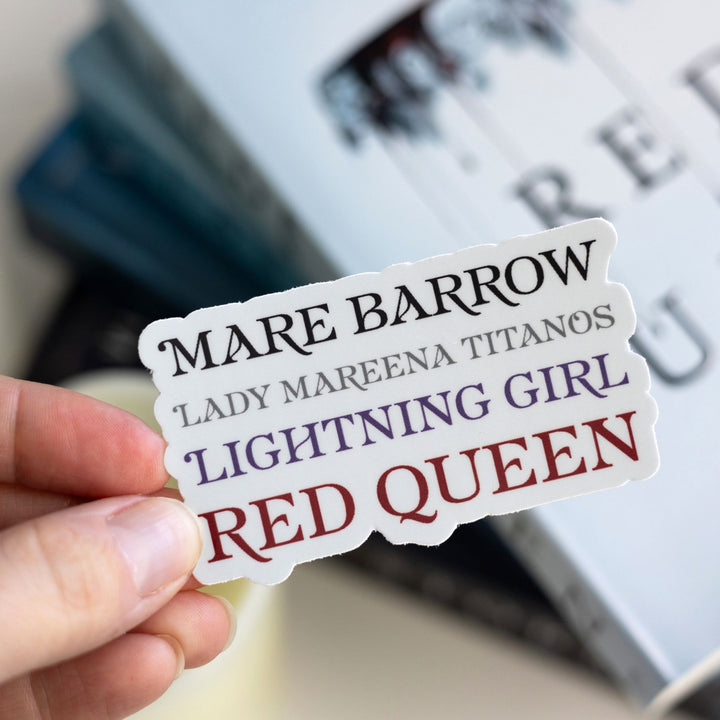 Sticker held over Red Queen. The sticker lists all the names for Mare Barrow in a stack. Text is ‘Mare Barrow, Lady Mareena Titanos, Lightning Girl, Red Queen.’