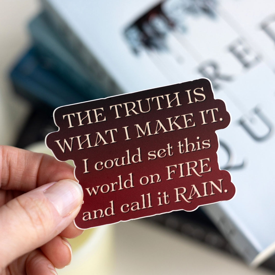 Quote sticker with tan text on a red background held over Red Queen. Text reads ‘The truth is what I make it. I could set this world on fire and call it rain.’