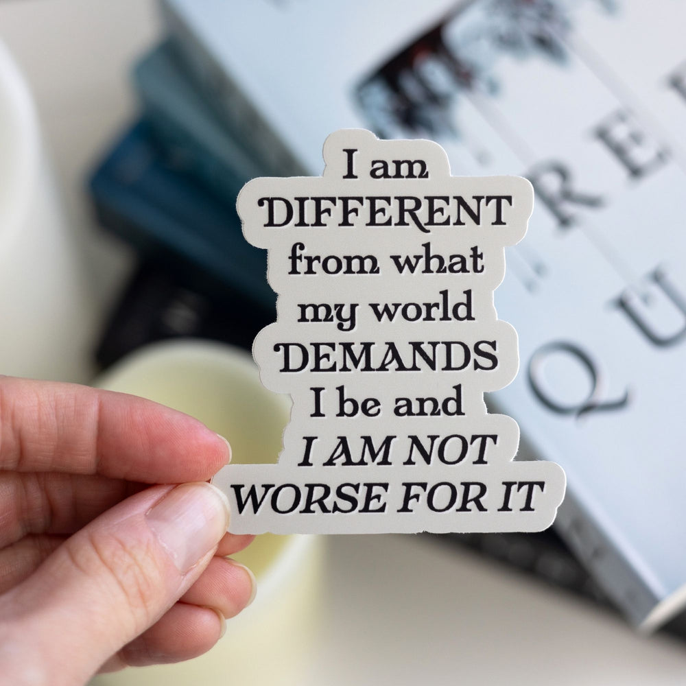 Quote sticker with black text on a grey background held over Red Queen. Text reads ‘I am different from what my world demands I be and I am not worse for it.’