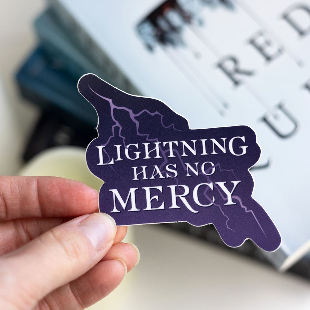 Quote sticker with white text on a purple background with a bolt of lightning held over Red Queen. Text says ‘Lightning has no mercy.’