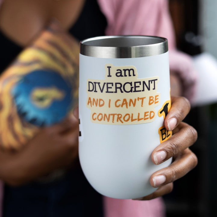 Quote sticker ‘I am DIVERGENT and I can’t be controlled’ on a white tumbler. Words are purple and gold. From Divergent by Veronica Roth.