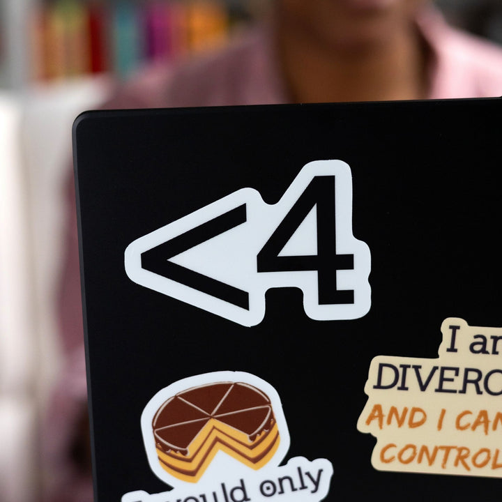 White sticker of the symbols < 4 in black on a black laptop. Funny sticker from Divergent by Veronica Roth.
